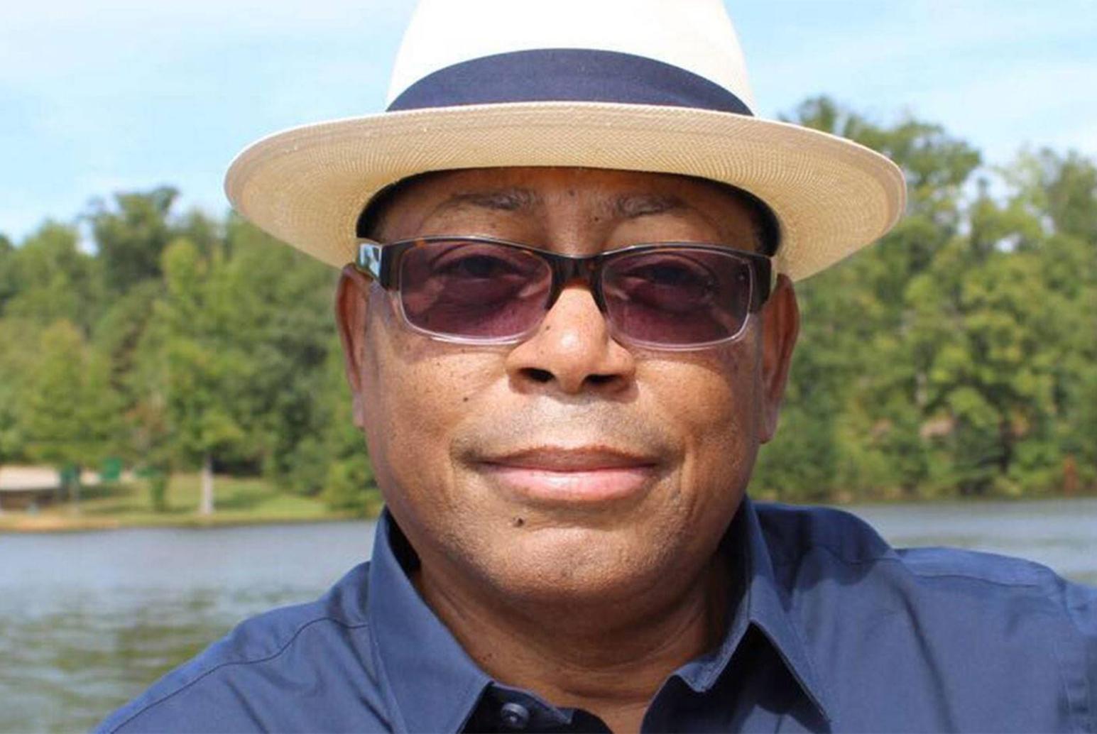 Close-up of Melvin Mann in dark blue shirt, sunglasses and straw fedora
