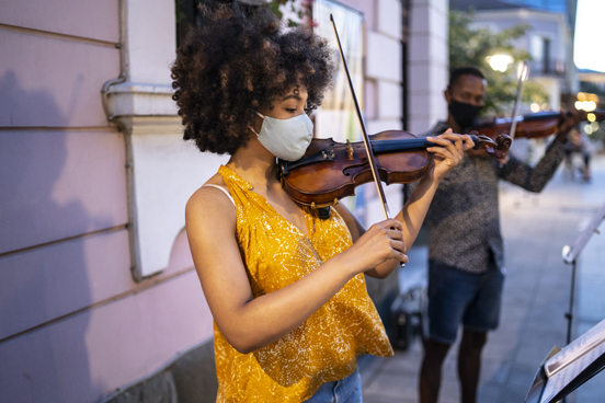 Two people playing violin on the street while wearing masks