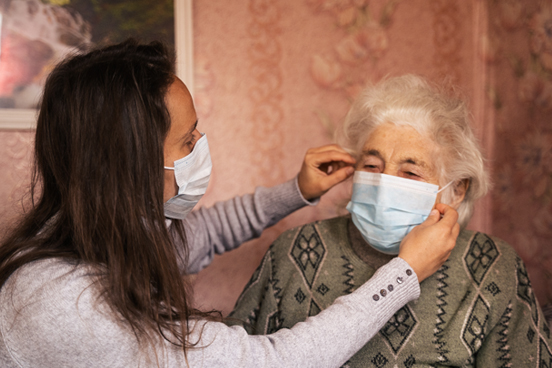 A masked person helping an elder put on a surgical mask