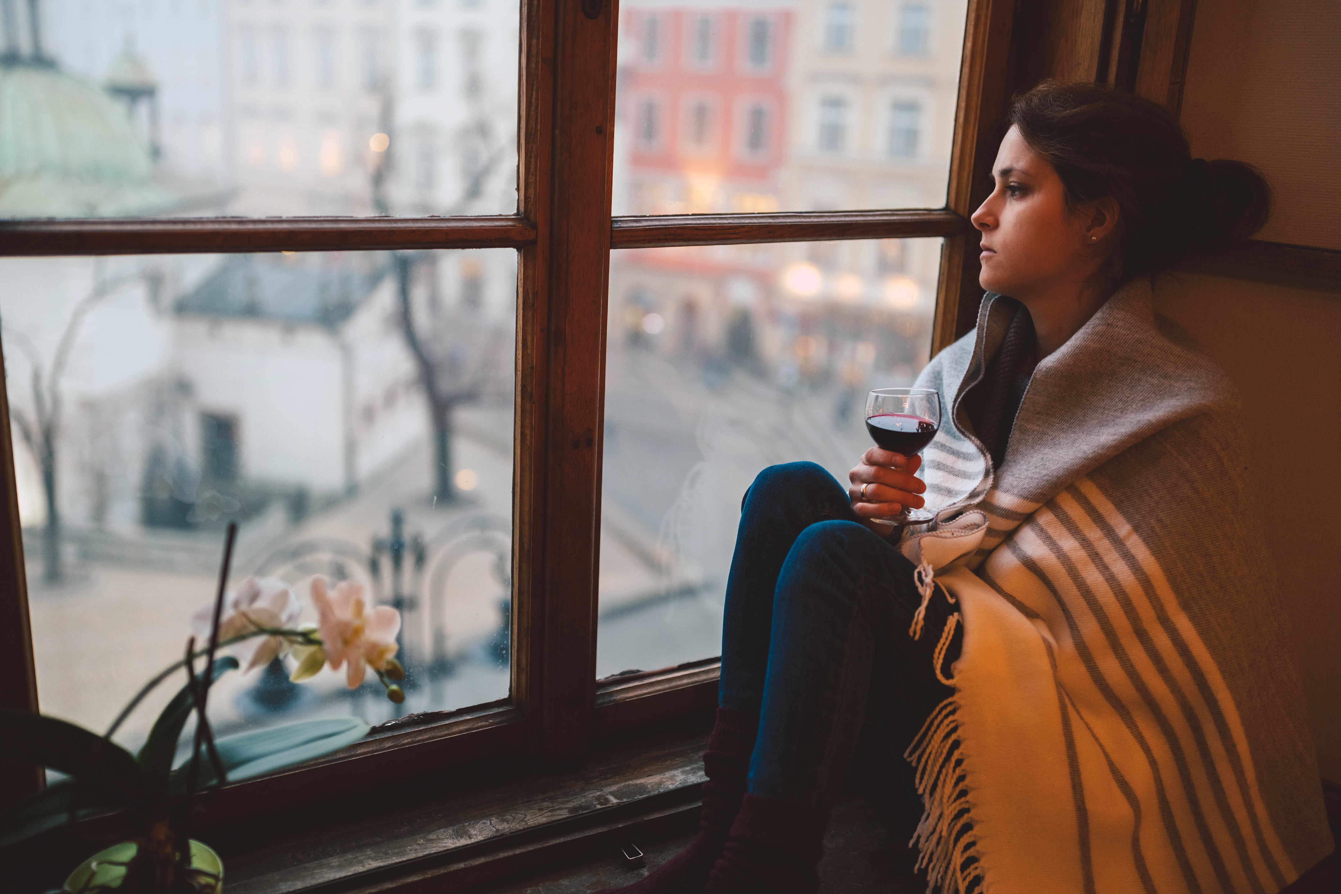 Person holding wine glass while looking out the window solemnly