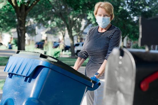 Woman with mask rolling out recycling bin