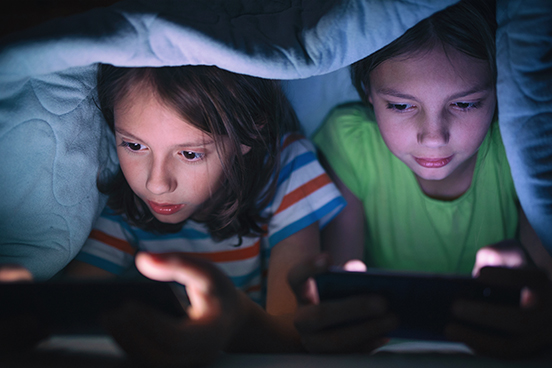 Two children on their phones under the blankets