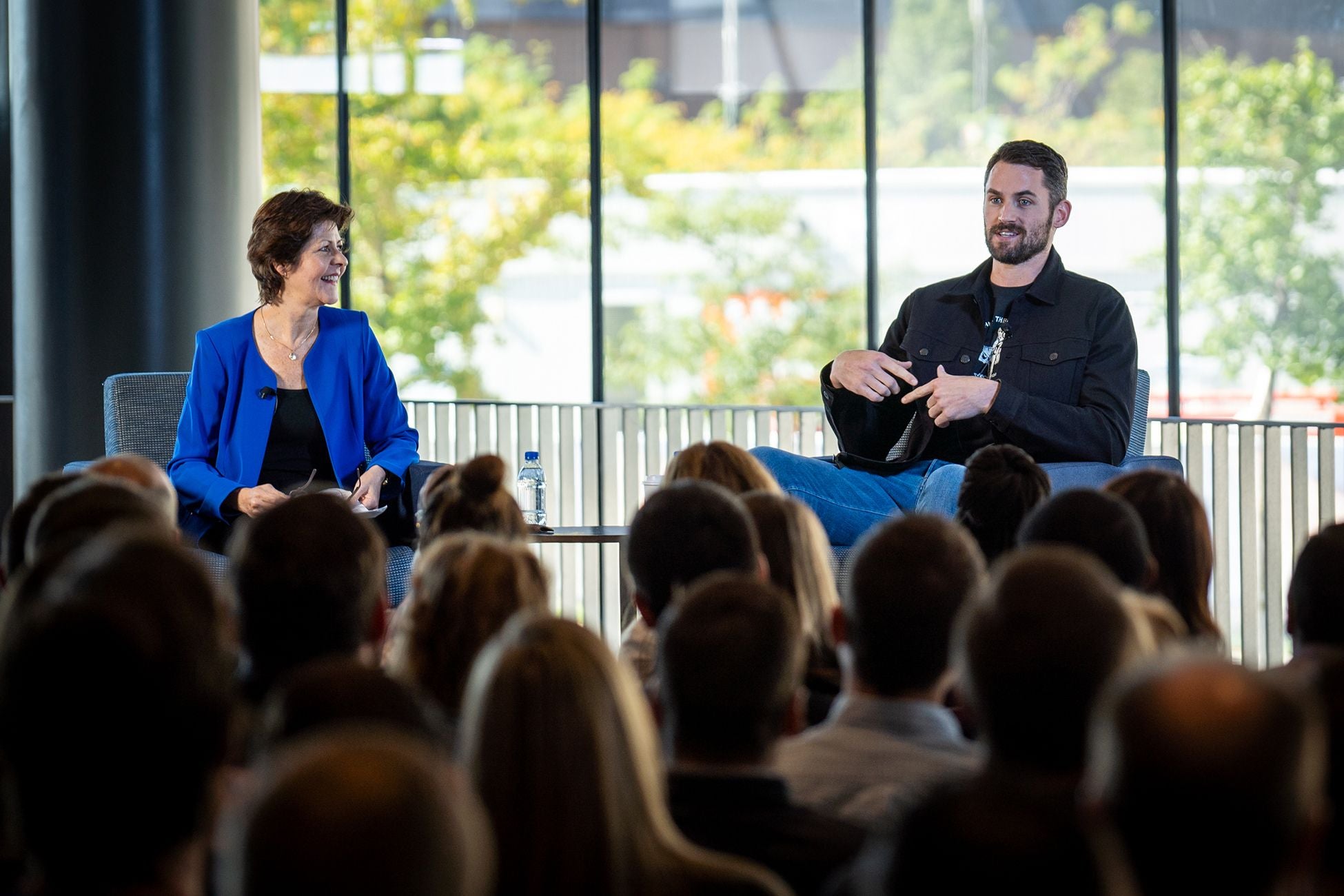 Woman and man sit in chairs on stage and speak to seated audience