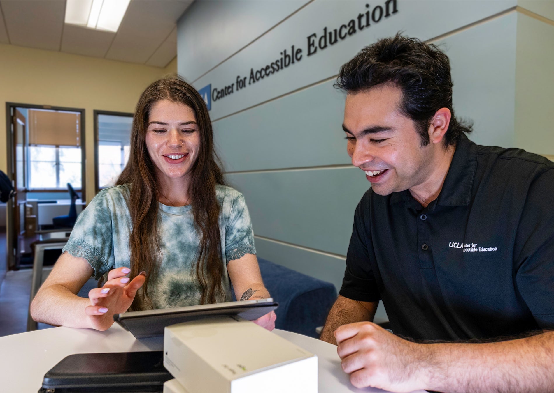 Female student and male staff member review information on tablet and smile