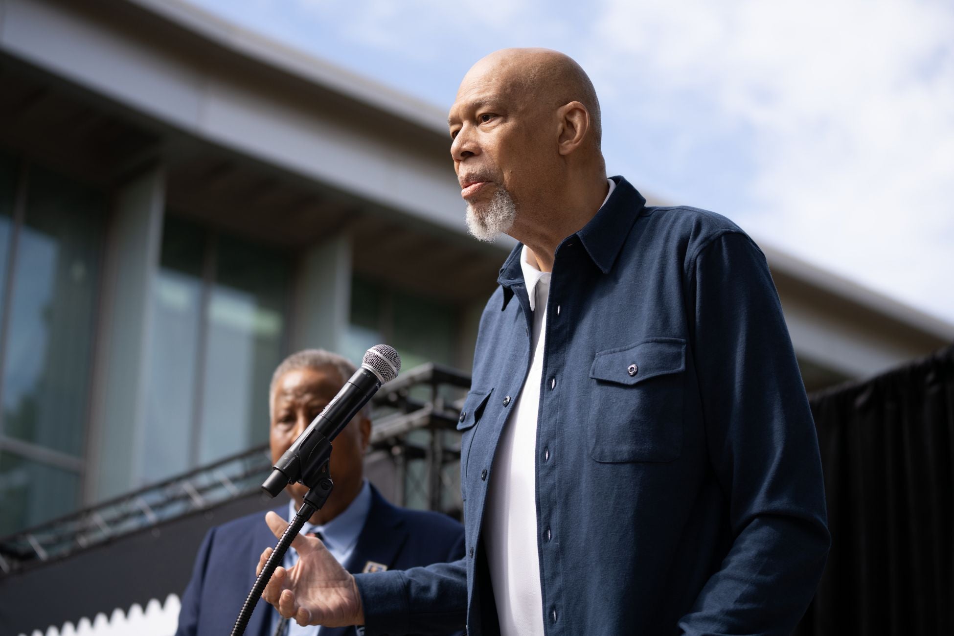 Kareem Abdul-Jabbar in a blue shirt and jacket speaks into a microphone during a presentation