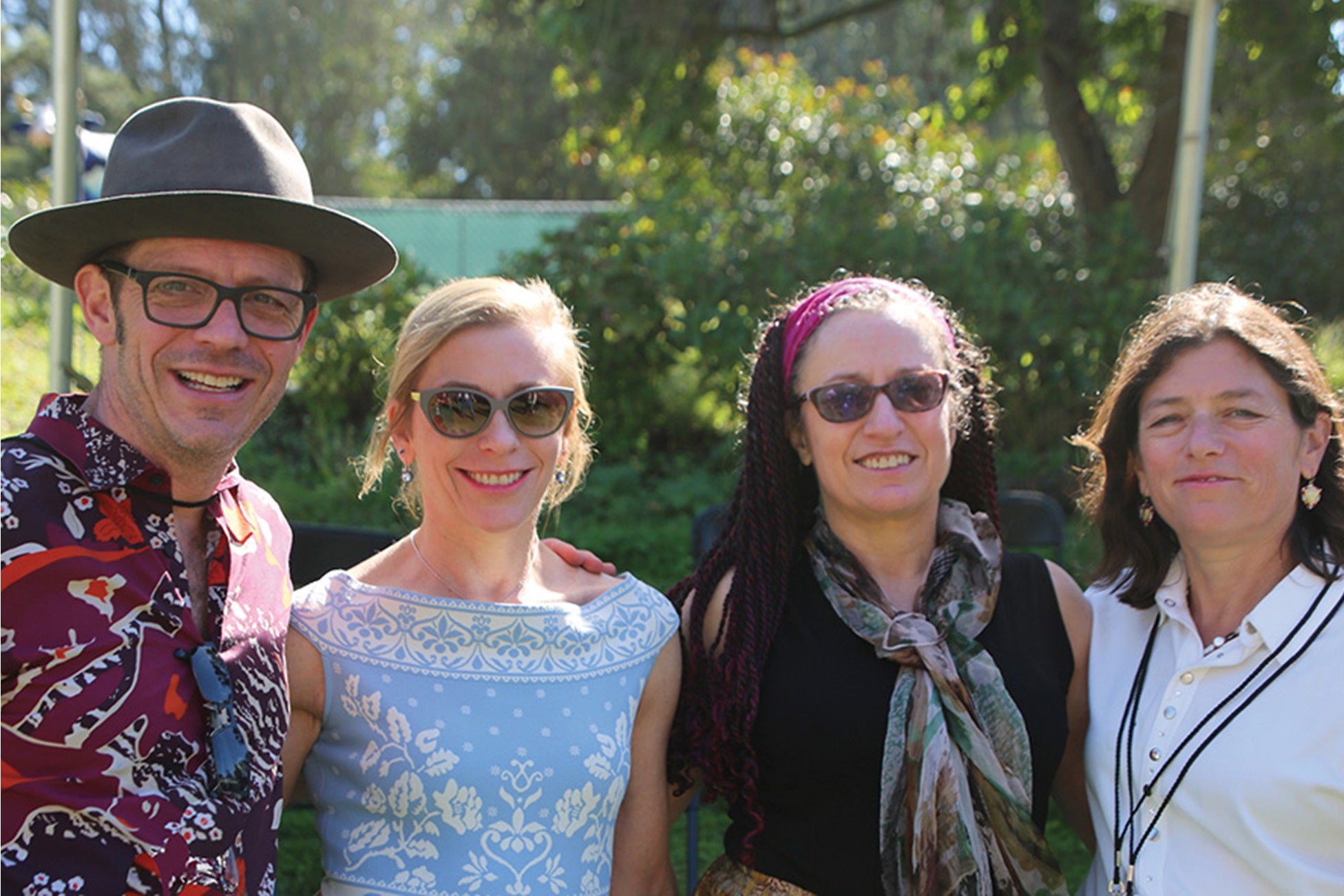 Man in hat and three women--one blonde, two brunette--smile to camera with arms around each other 