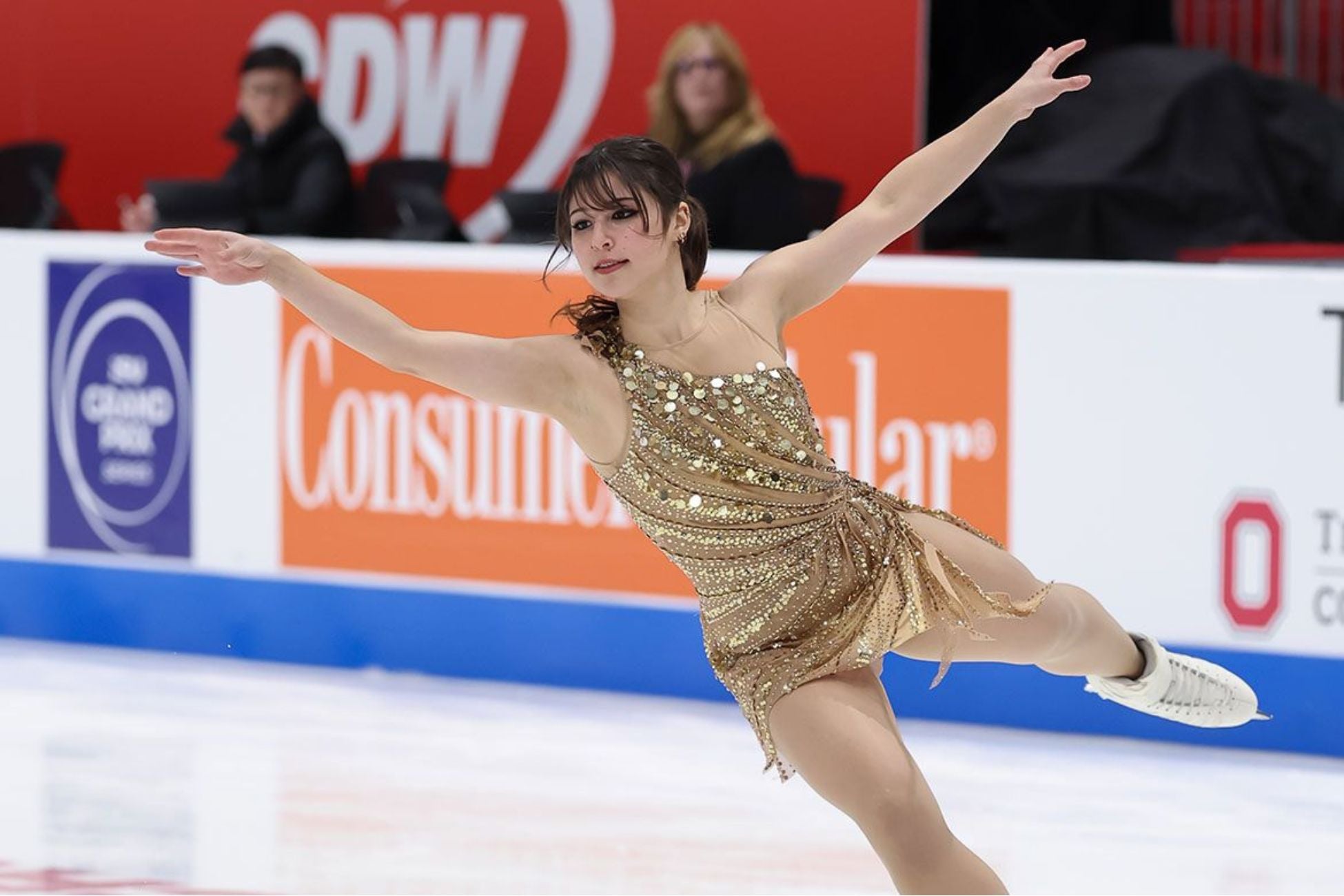 A woman wearing a gold outfit skating on an ice rink