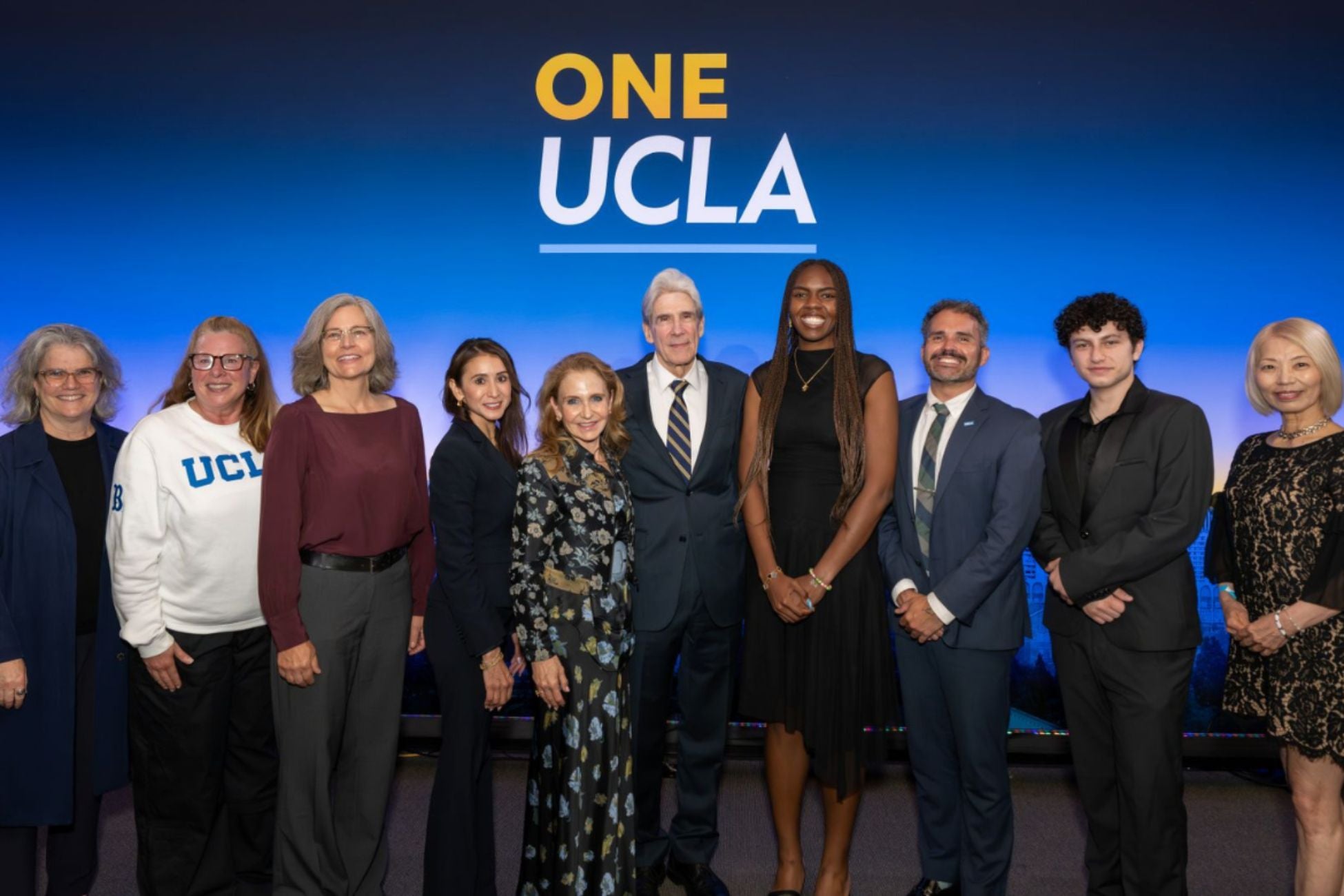 UCLA community members gathered and smiling in front of a backdrop that reads "One UCLA". 