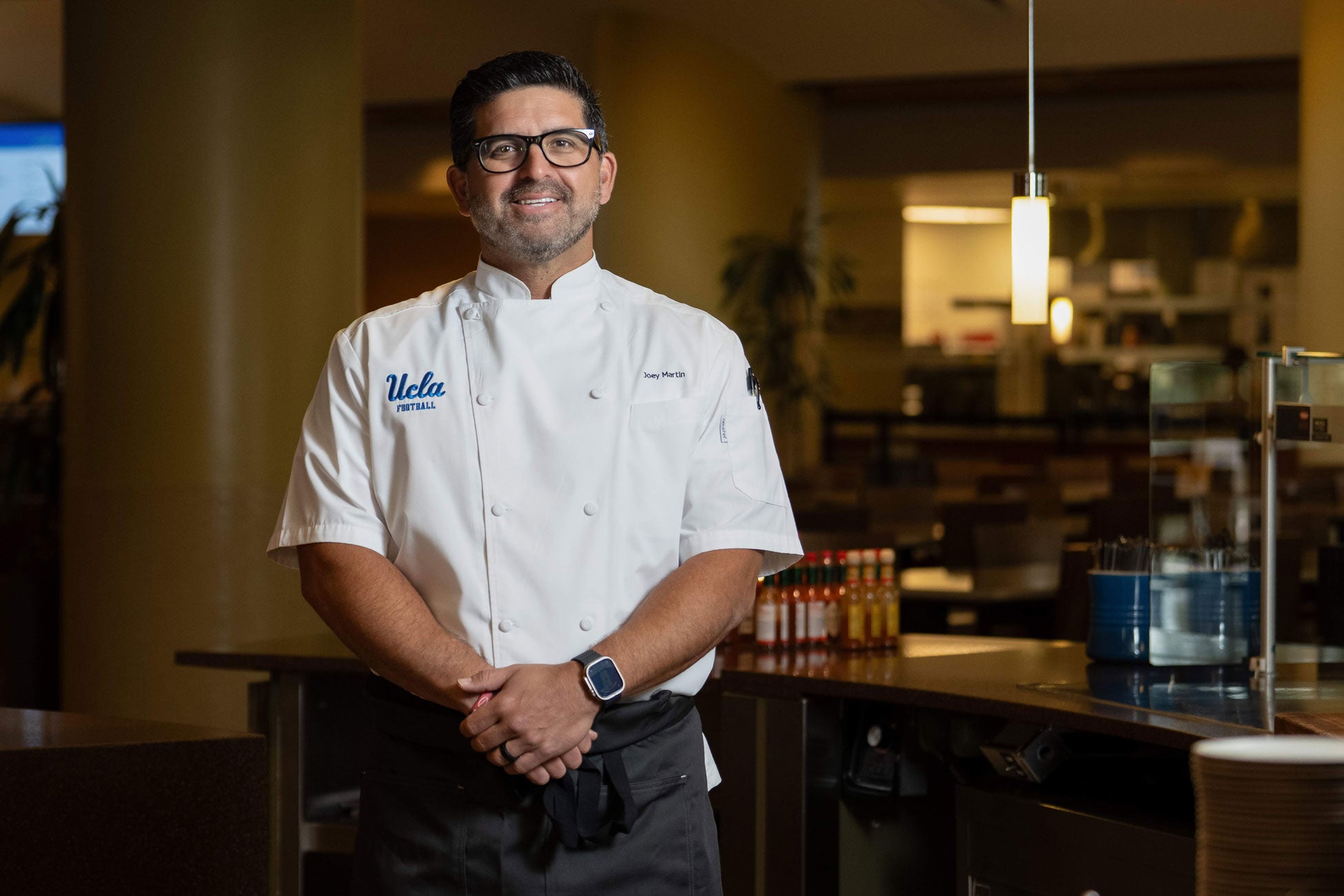  A chef wearing a white shirt and glasses stands confidently with a light blue, shining background.