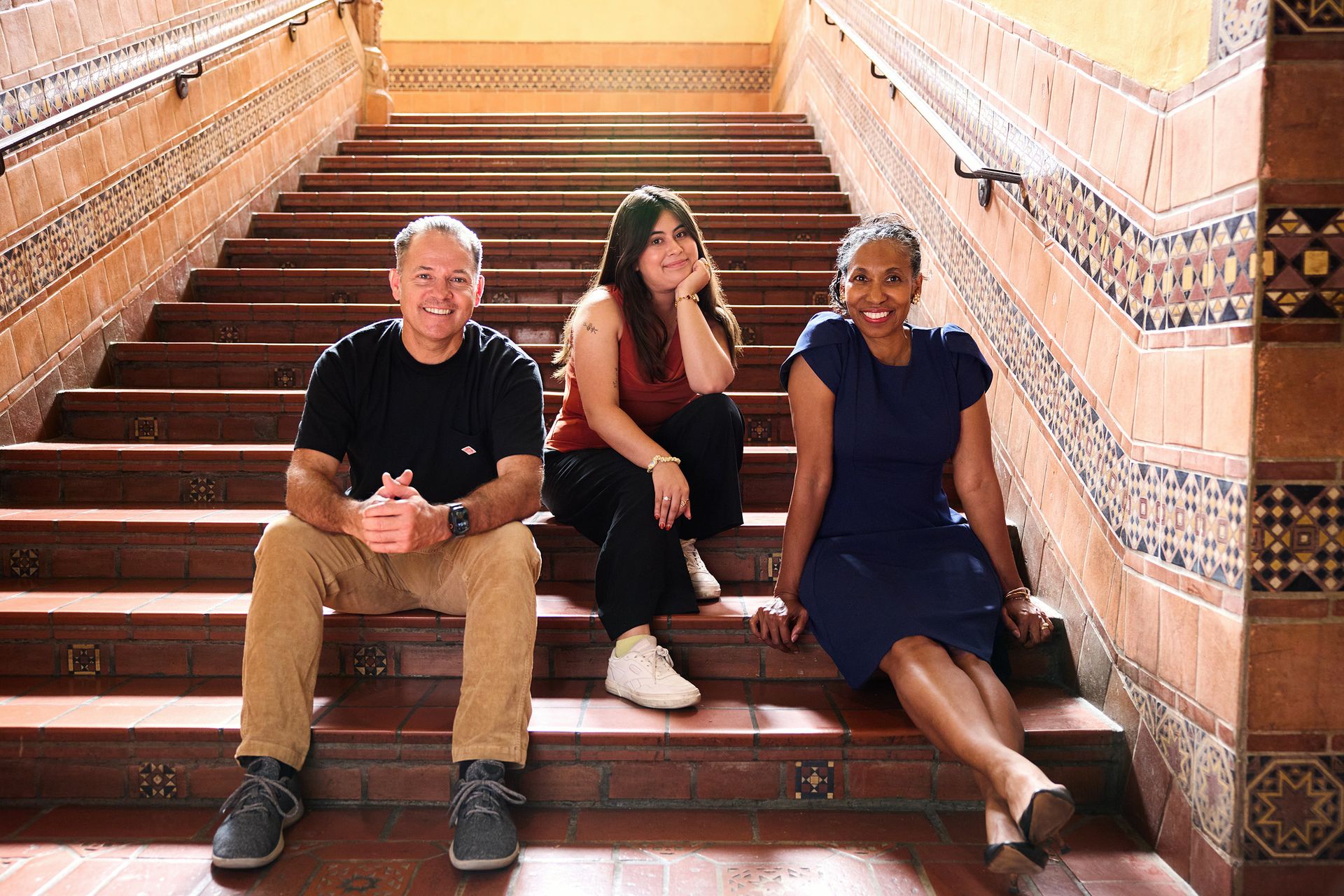 " Three individuals seated on the stairs of an old building, surrounded by historic architecture and textured walls. "