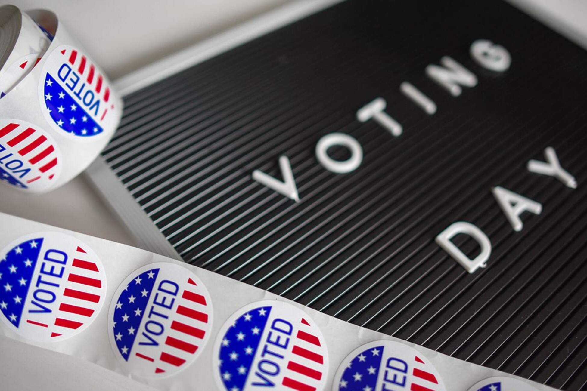 Red, white and blue "I Voted" stickers next to a black-and-white "Voting Day" sign.