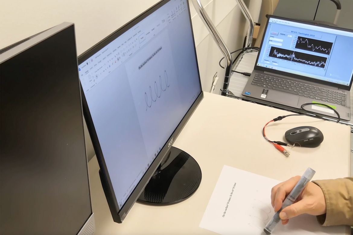 Hand holding pen as a monitor mirrors the letters written on paper