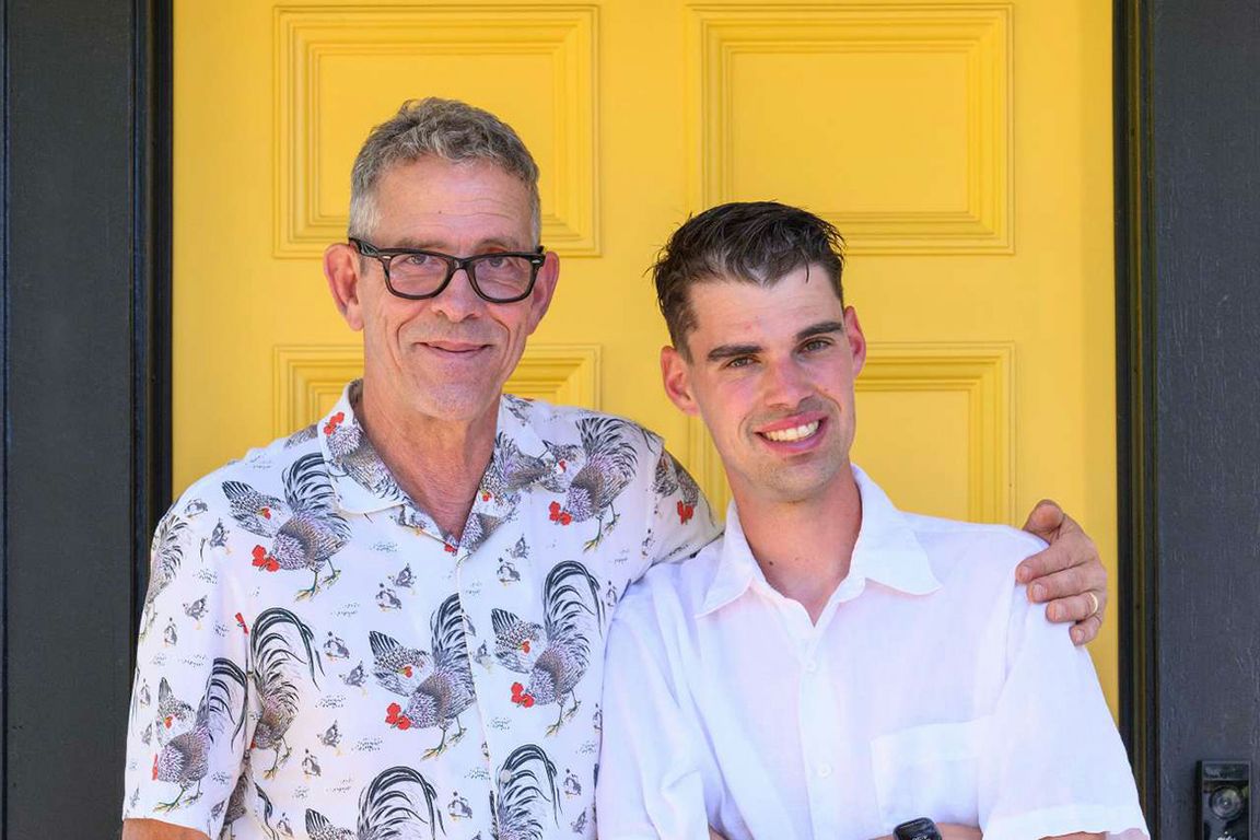 Son and father stand smiling in front of a yellow door
