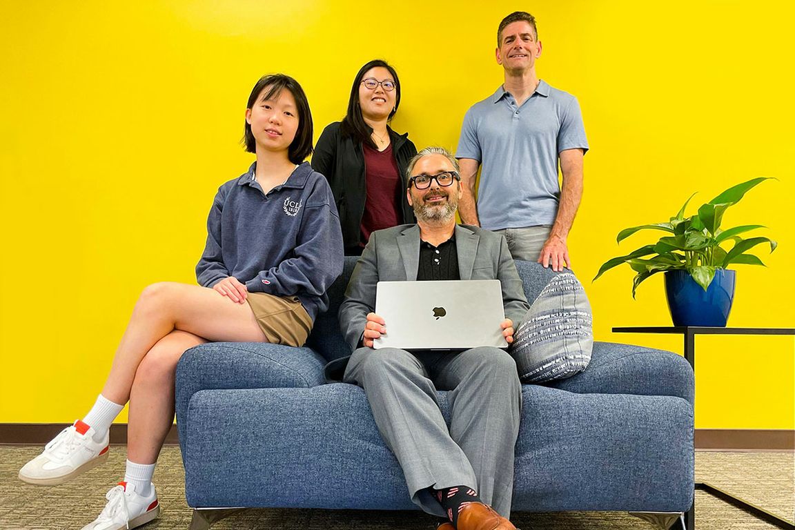 Four people sitting and standing around a couch with a yellow back wall
