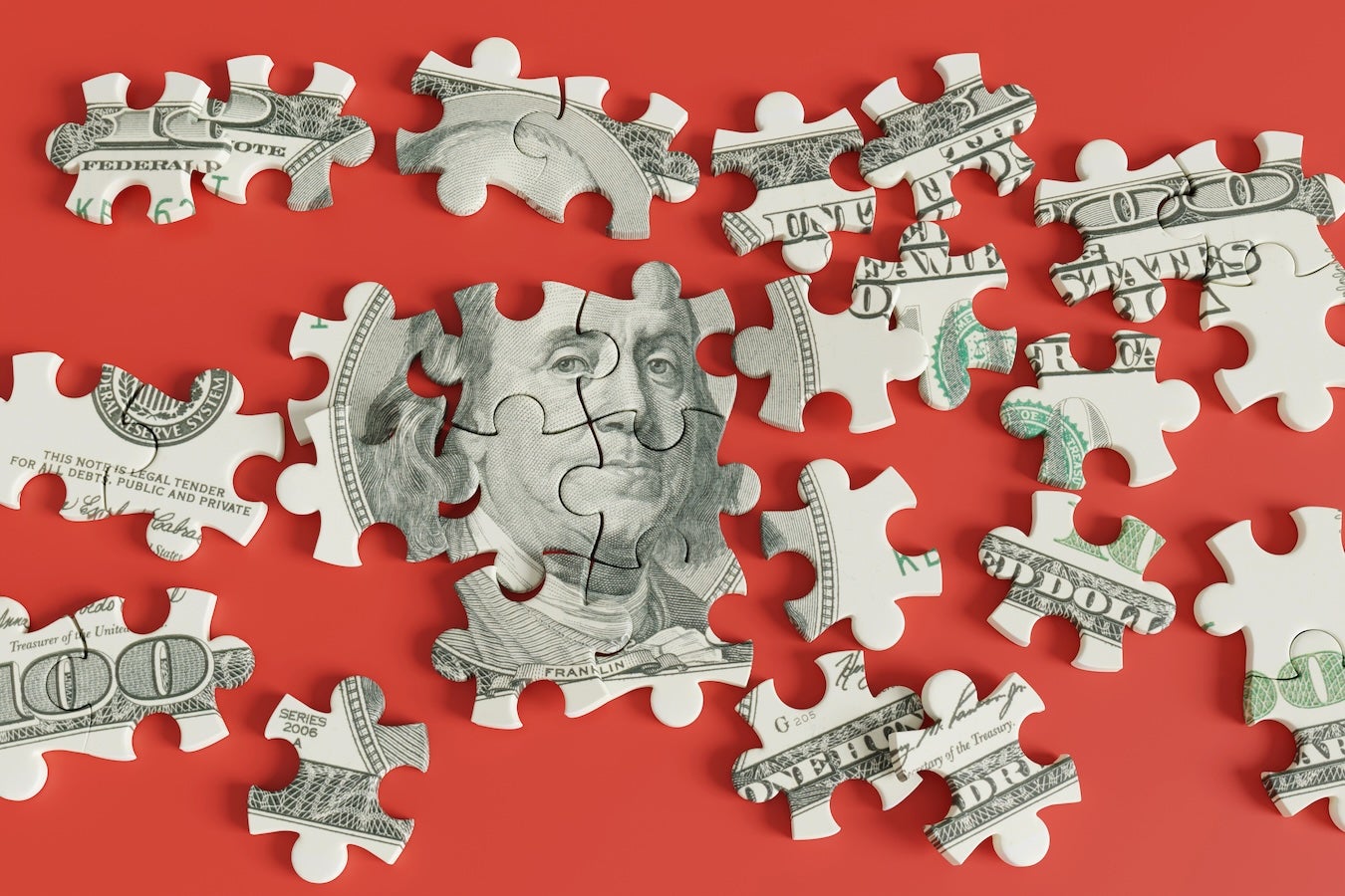 Puzzle pieces of $100 bill show Ben Franklin's face against red background