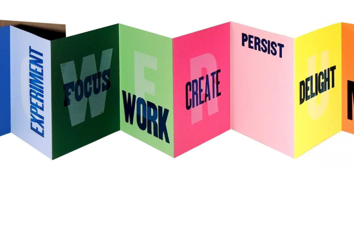 A series of colorful, folded panels arranged in a zigzag formation, featuring bold words including “EXPERIMENT,” “FOCUS,” “WORK,” “CREATE,” “PERSIST,” and “DELIGHT.”