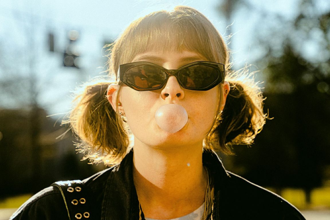 Close-up of woman with pigtails and sunglasses blowing a bubble with gum
