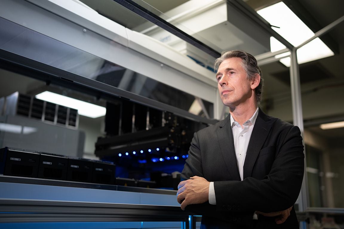 Robert Damoiseaux, in black jacket and white button-down, standing next to large device