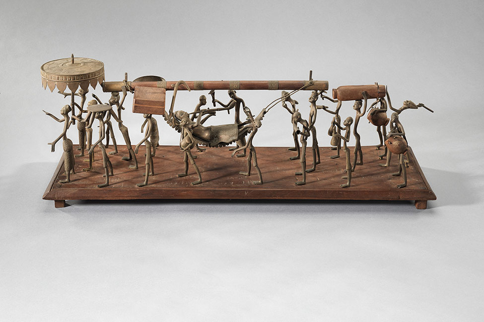 A sculpture of approximately 20 small brass figures in a procession, attached to a wood plinth