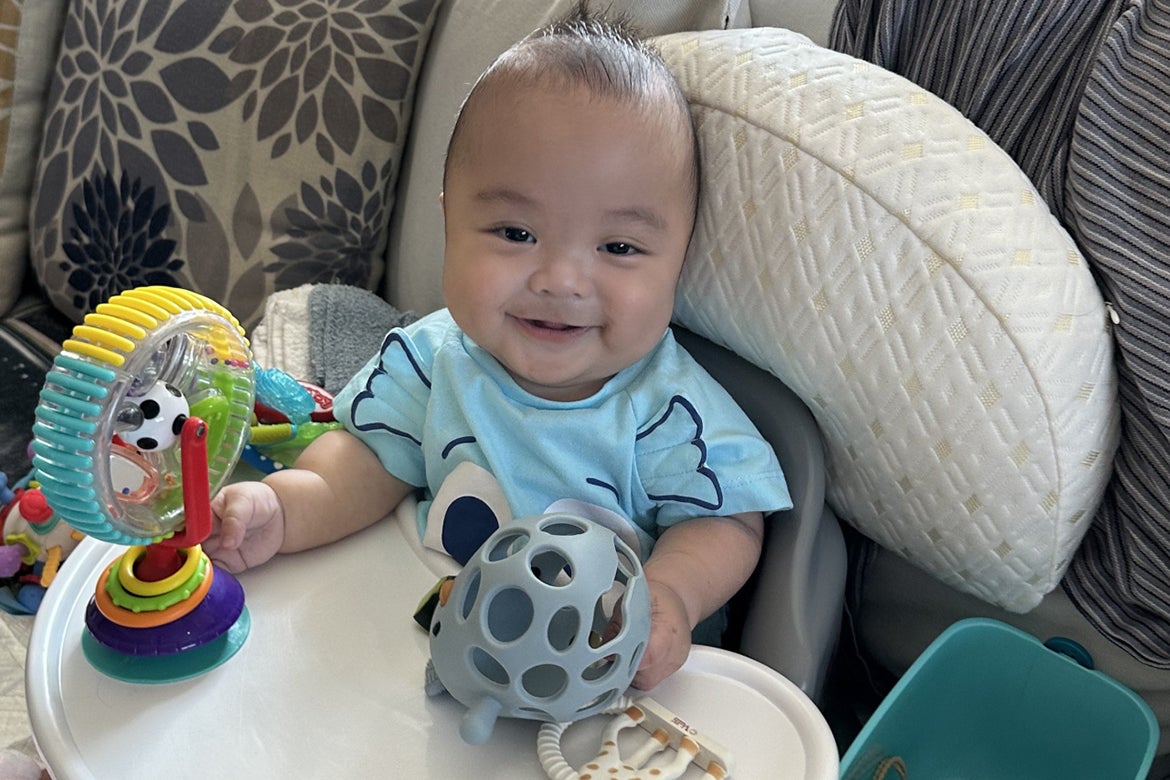 Smiling baby in light blue holding toys in both hands