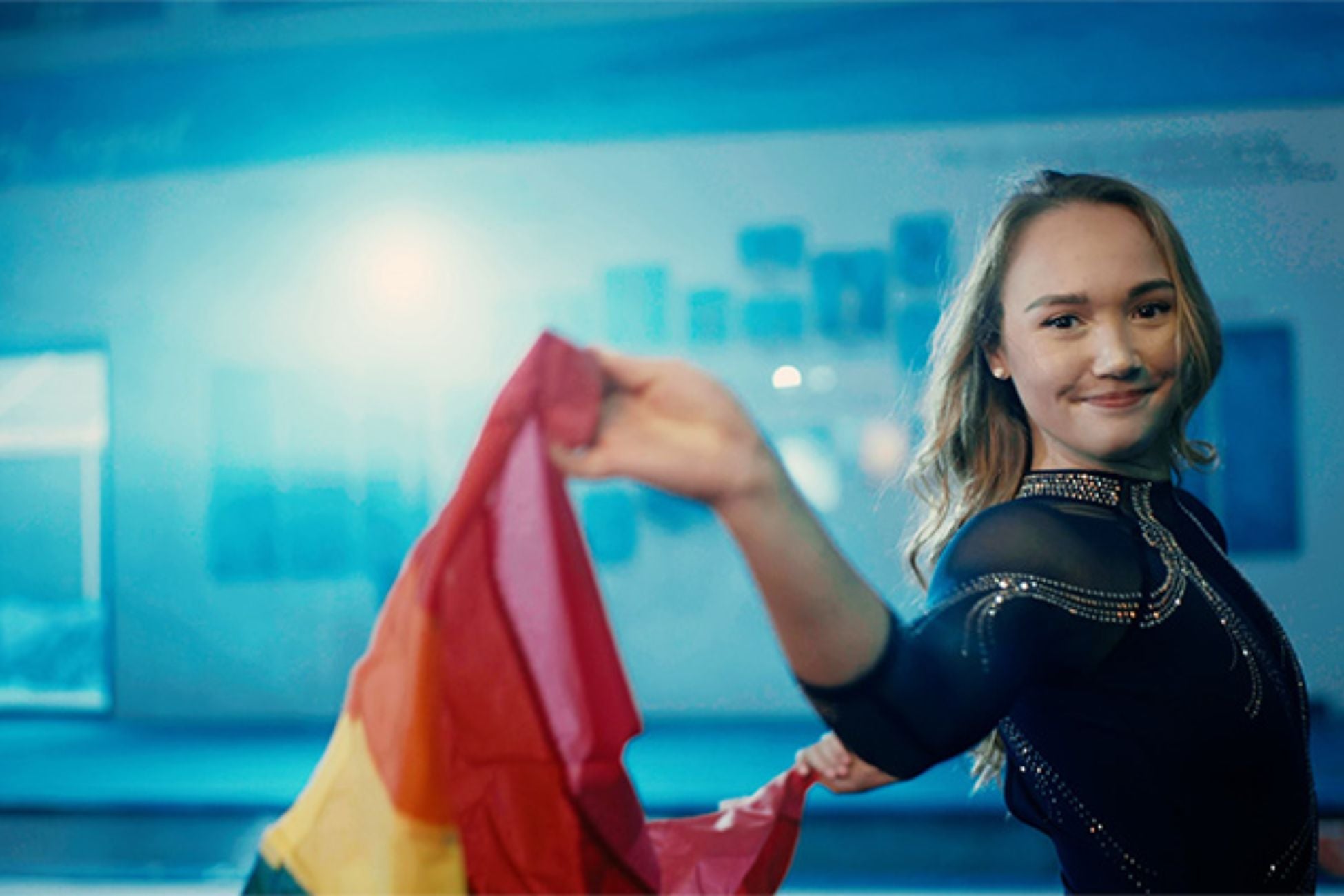 UCLA gymnast stands holding a vibrant rainbow flag