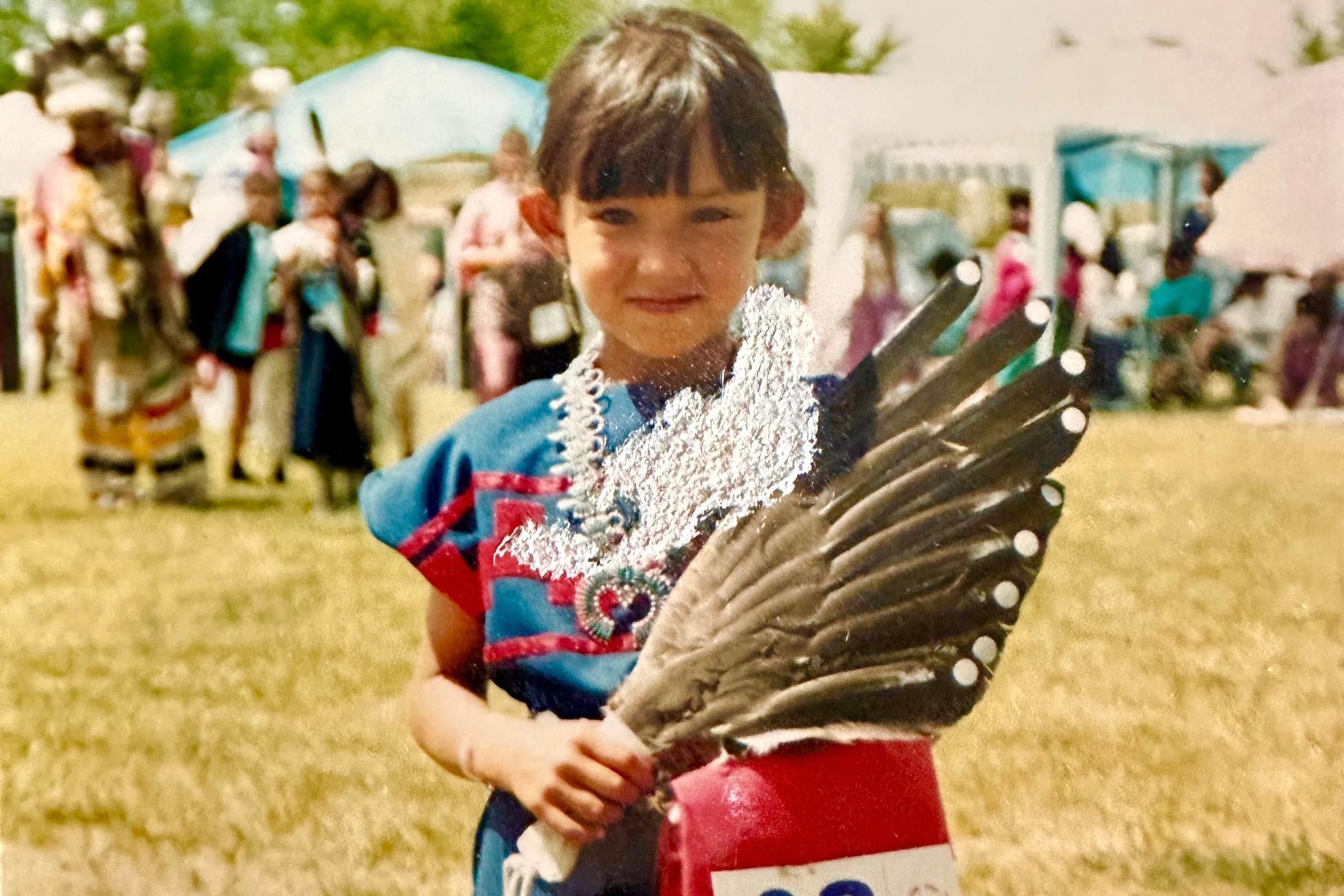 A young girl wearing a native dress holds a feather