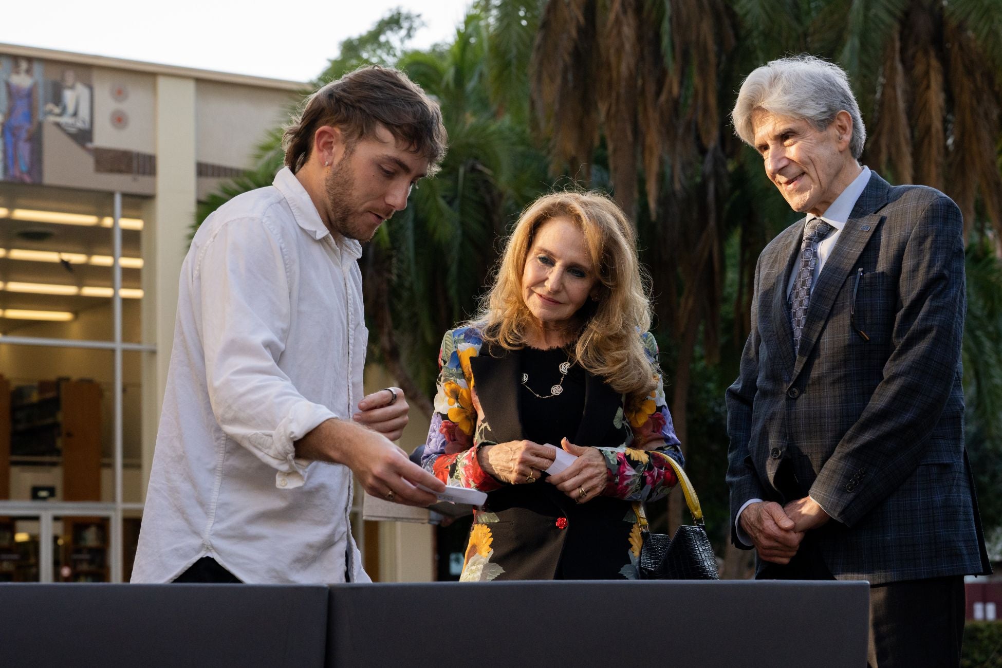 A student sprinkles seeds into a planter, while Chancellor Frenk and Felicia Knaul watch