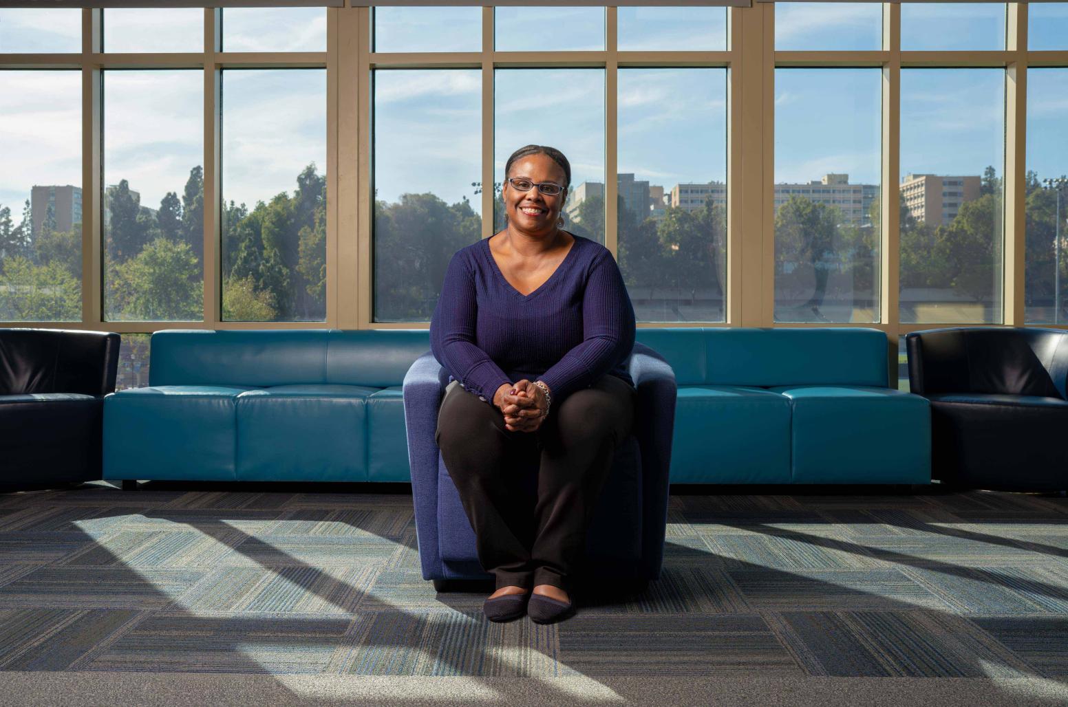 Nicole Presley, in blue shirt and black pants, seated in a blue armchair