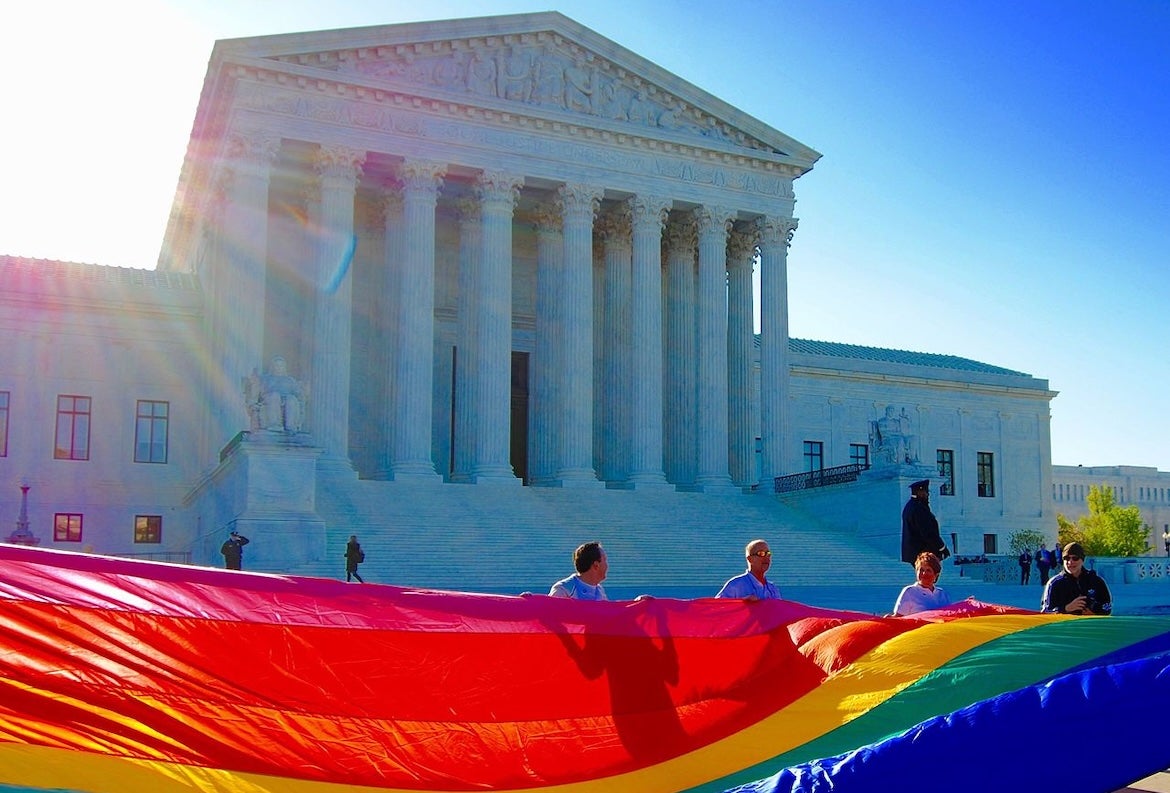 Yards-long rainbow flag is held up by four people below the front steps of the U.S. Supreme Court