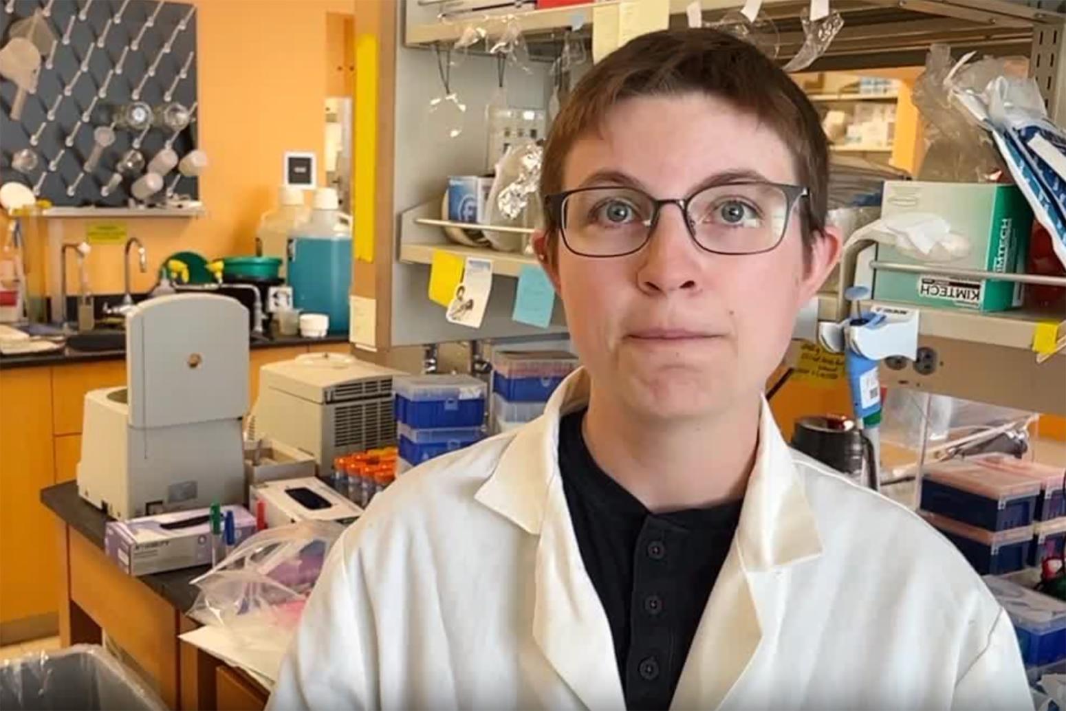 Head-and-shoulders photo of OIivia Justynski wearing lab coat and glasses in a lab 