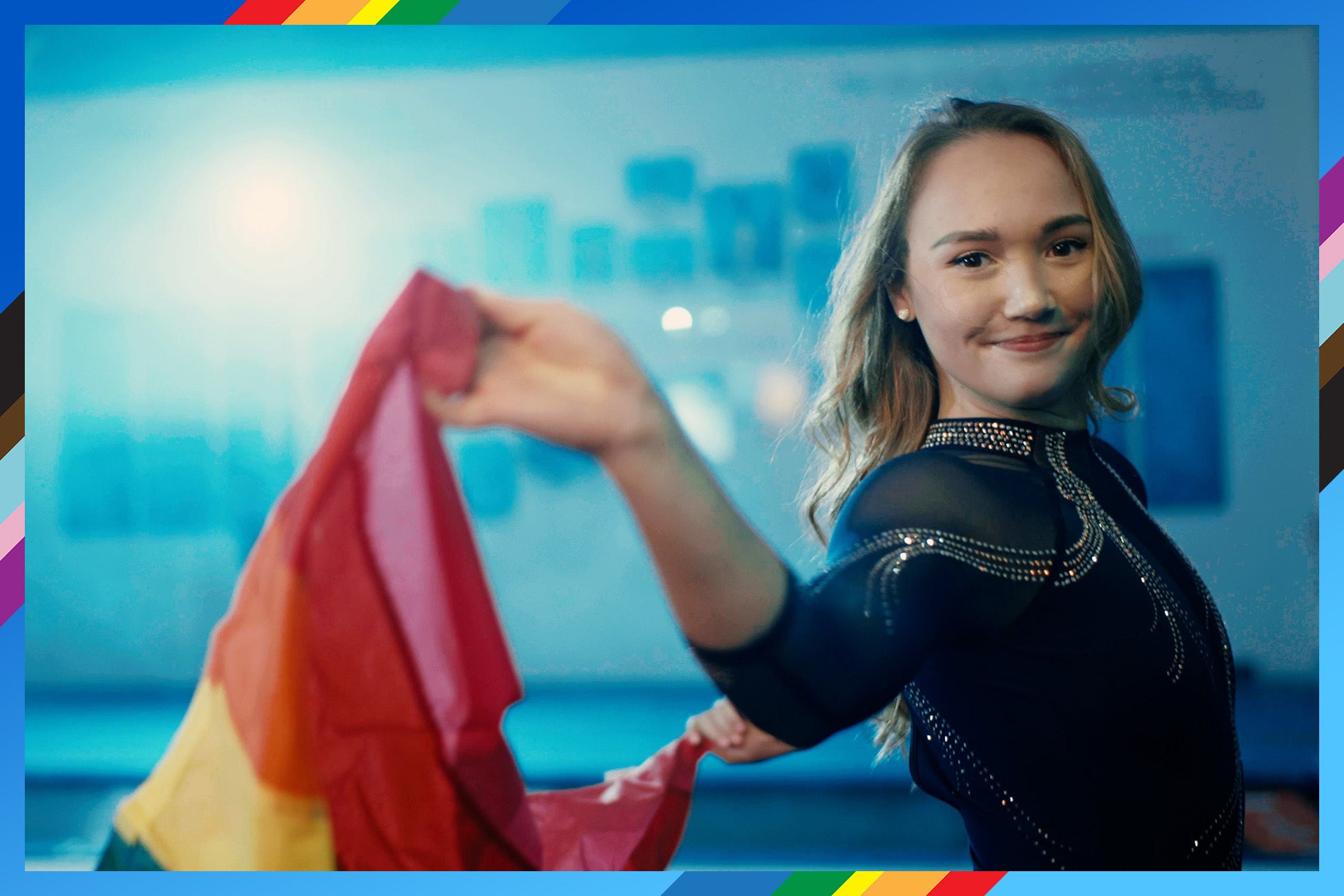UCLA gymnast stands holding a vibrant rainbow flag