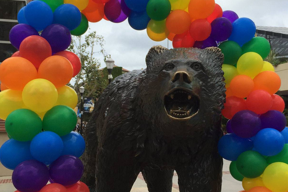 Statue of the UCLA Bruin with an arch of grouped red, orange, violet, blue, green and yellow balloons to represent a rainbow