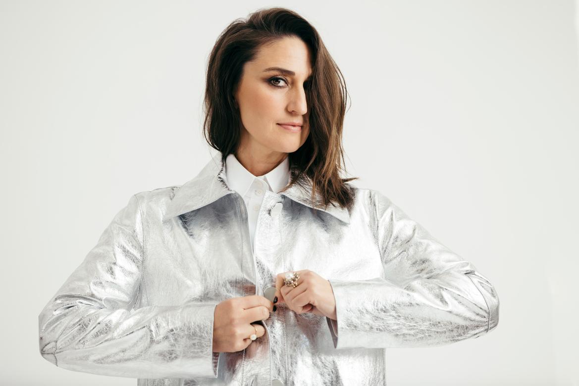 Sara Bareilles with long bangs covering left eye as she buttons a silver jacket