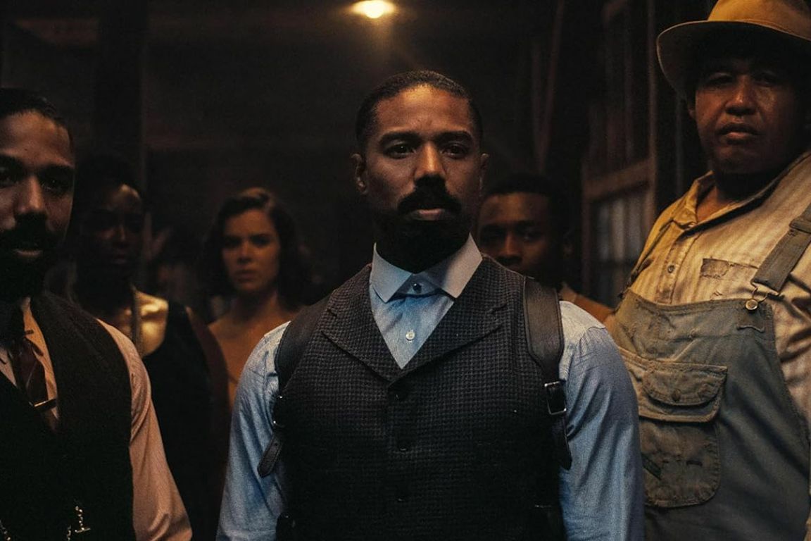 Image from "Sinners" of man in vest with several characters behind him