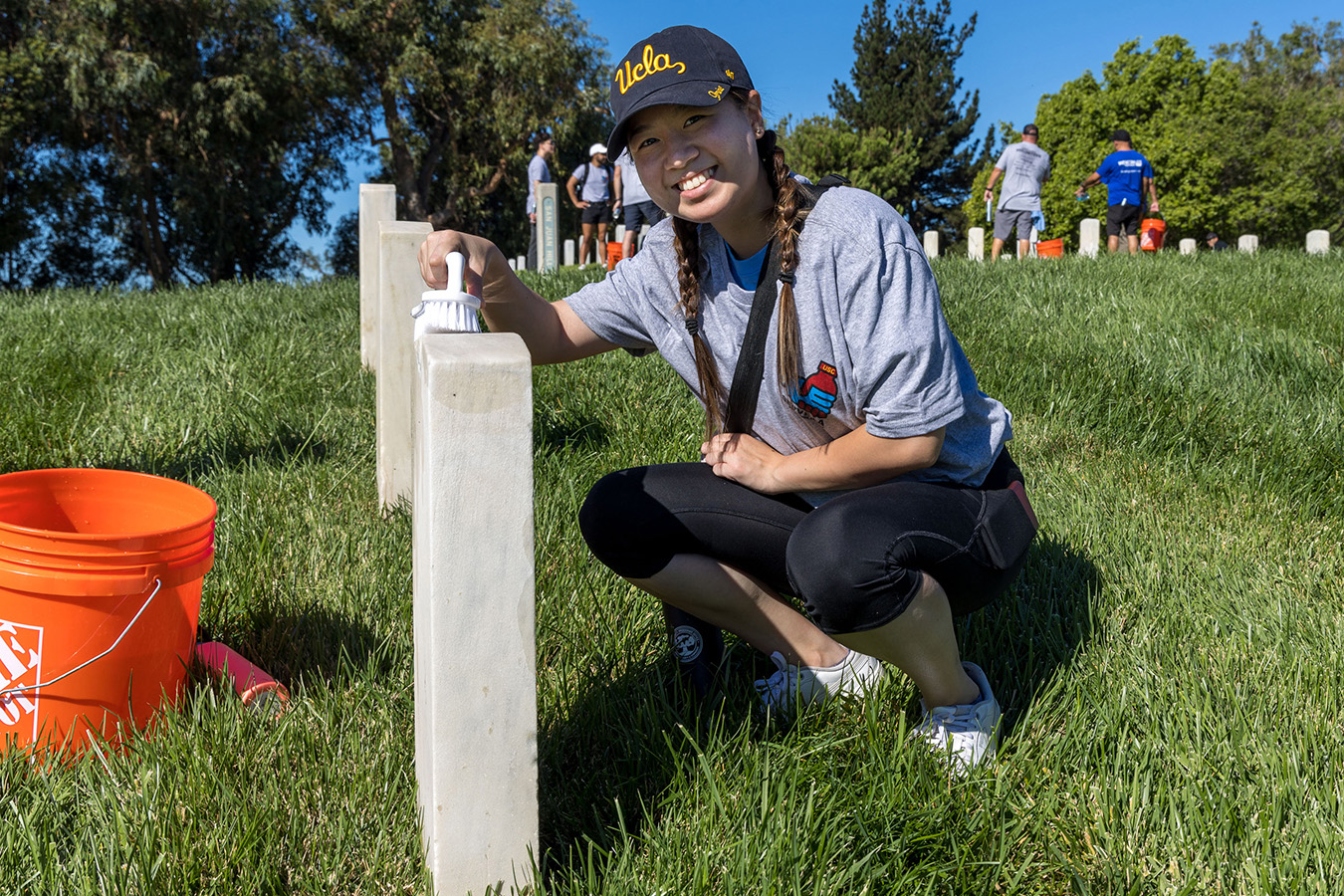 Woman UCLA student scrubs a headstone at the Los Angeles National Cemetery