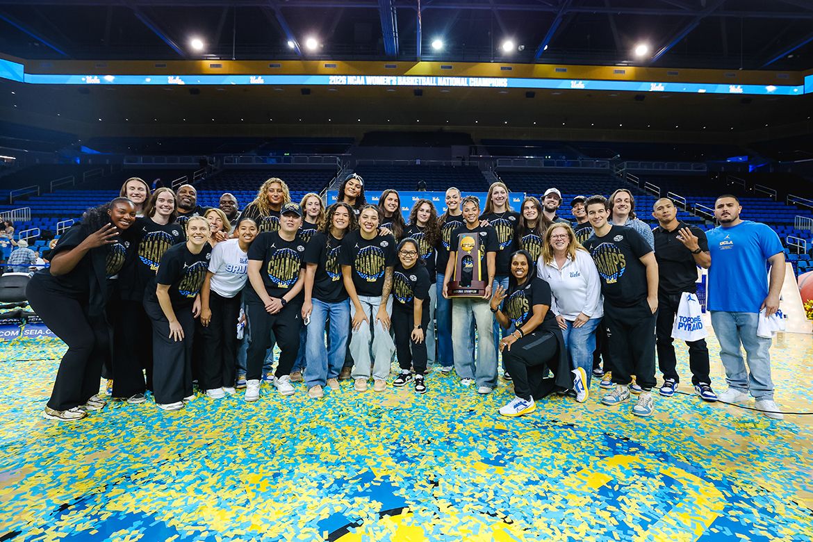 The UCLA women's basketball players, coaches and staff celebrate on a confetti-strewn court floor