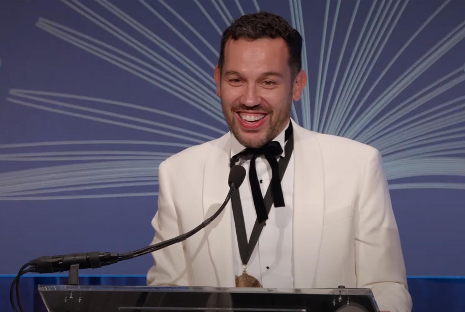 Justin Torres at podium in a white jacket giving speech at National Book Awards ceremony