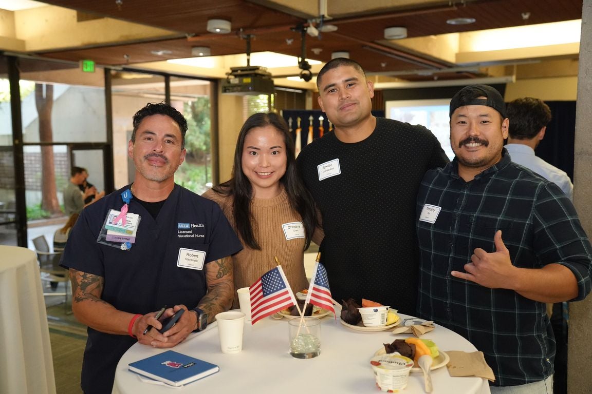Four people stand around a round table with two small flags on it