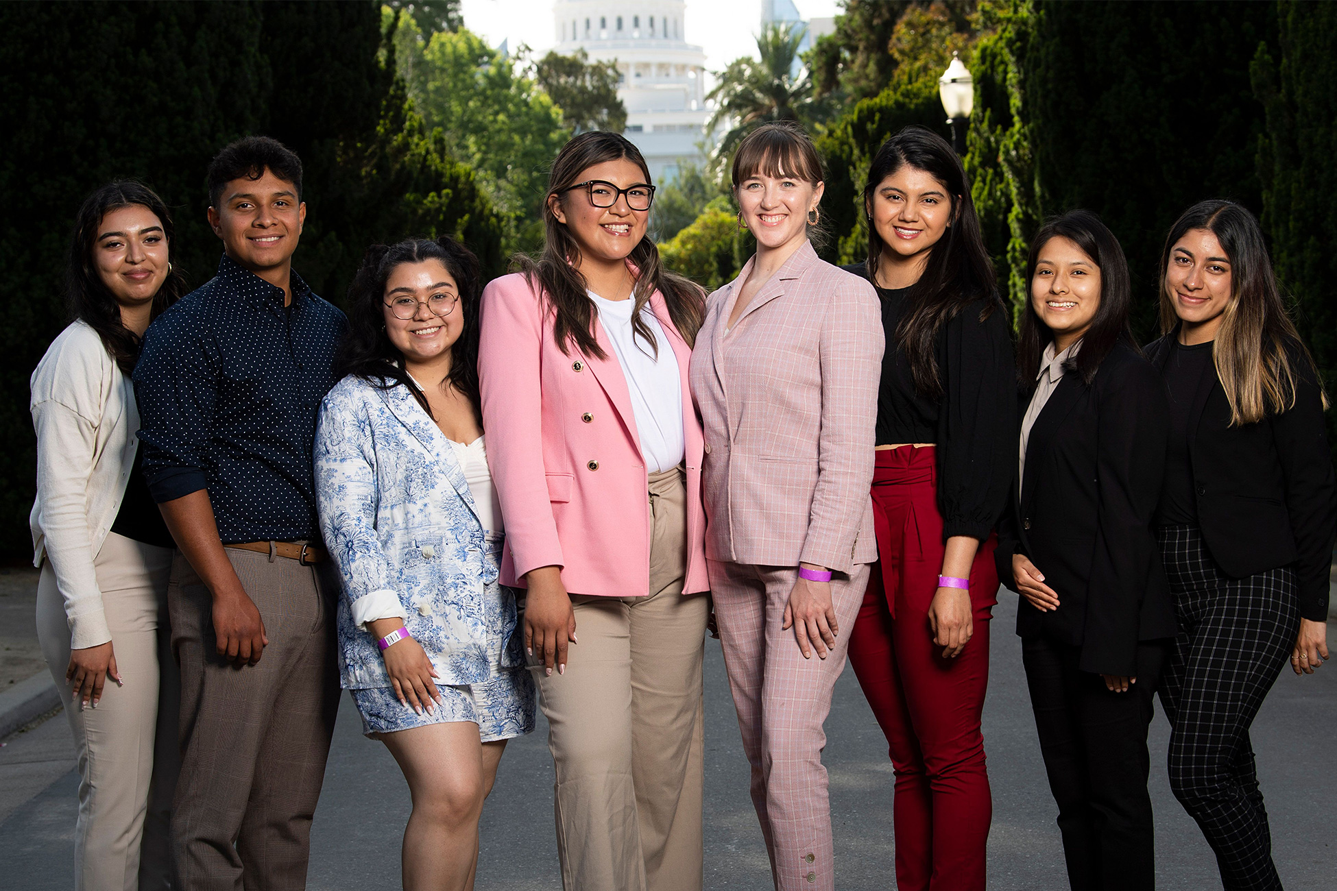 Seven Latina women and one Latino man stand with the California State Capitol in the background 