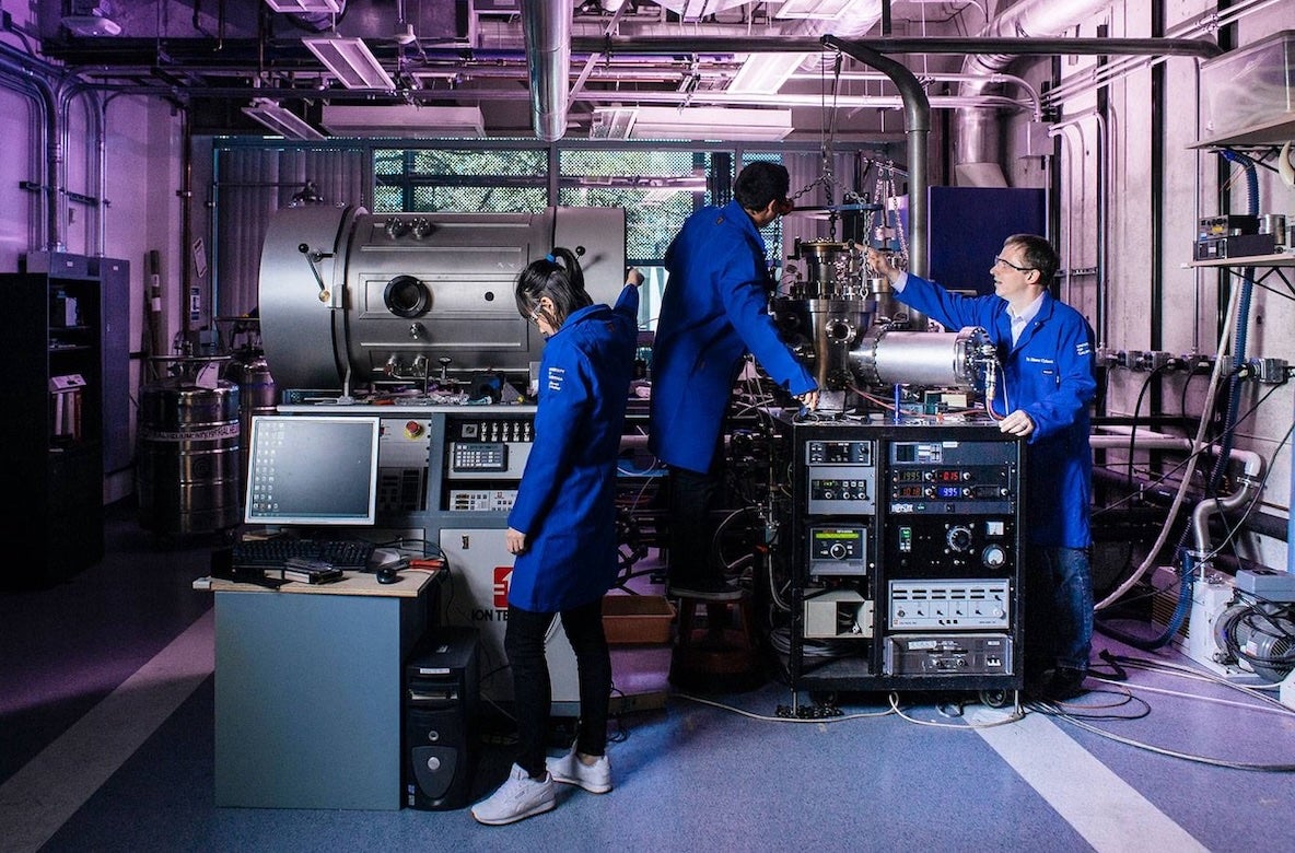 Scientists in blue coats working with machinery in a lab