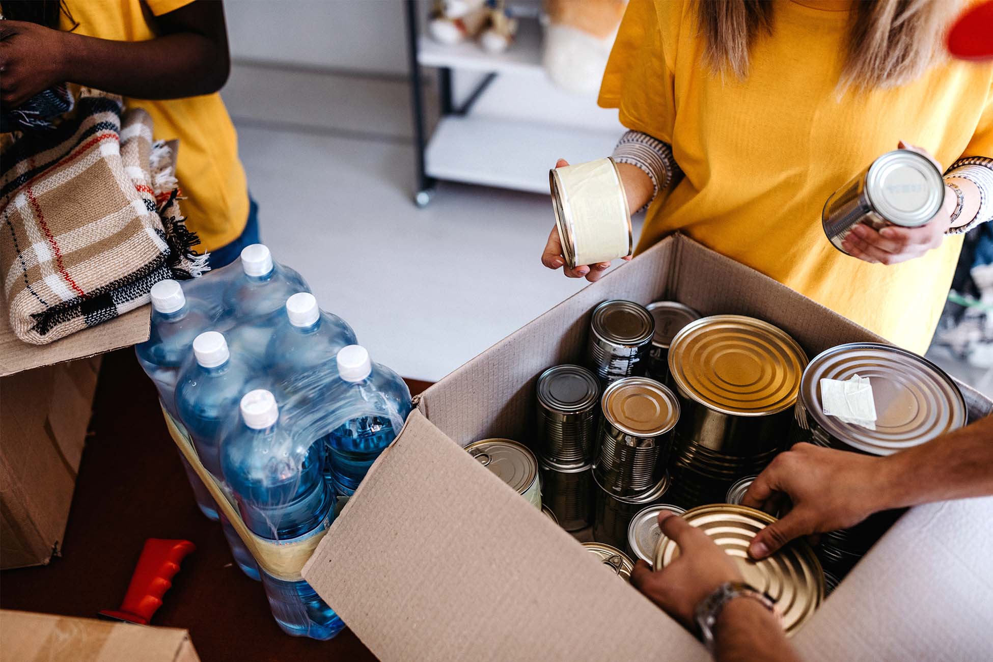 People wearing yellow shirts add canned goods and other items to a box.