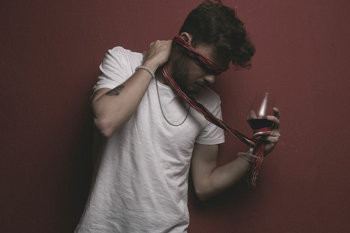 Man wearing white T-shirt and blindfold holding glass of wine in one hand