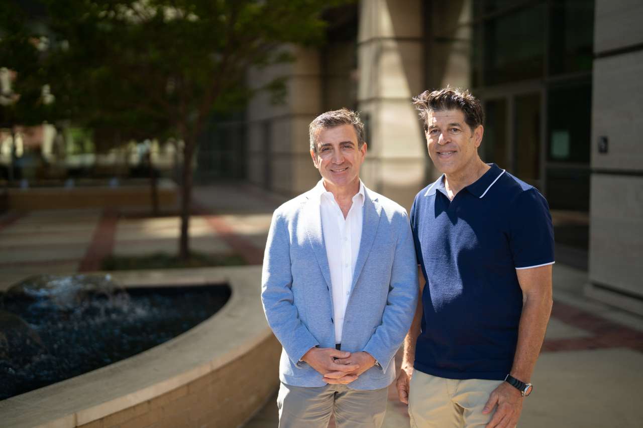 Drew Moghanaki,left, in light blue jacket and white shirt, stands with Paul Hendrix, in dark blue top, next to a water fountain