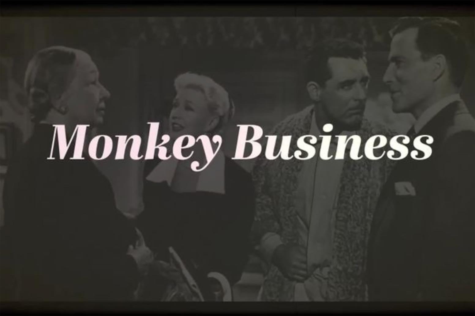 Black-and-white image of four people standing together talking; "Monkey Business" overlaid across image