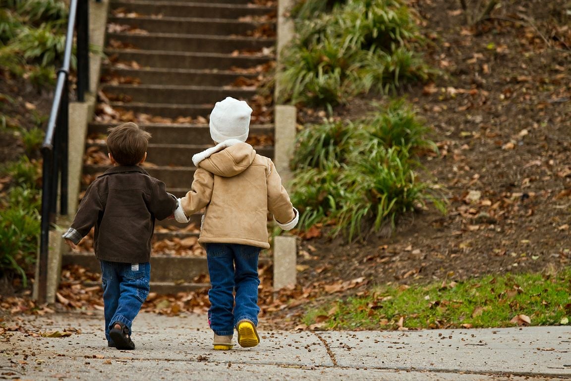 Two children in jeans and coats, holding hands as they walk