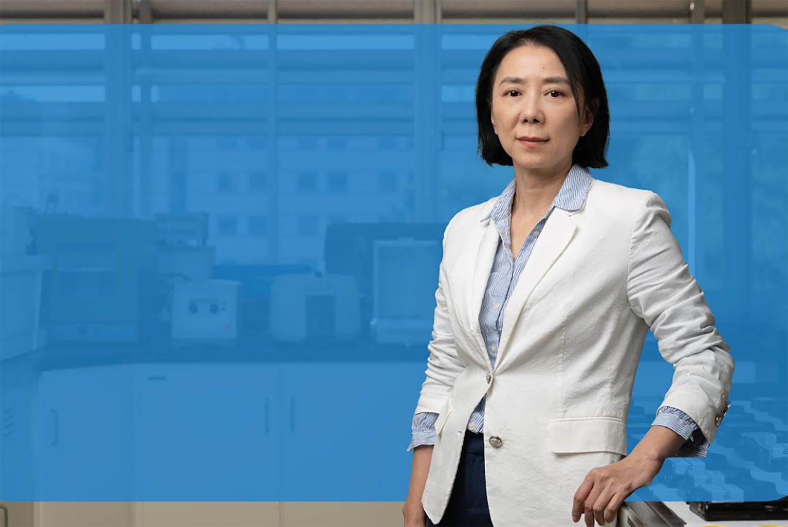 Yifang Zhu, in white blazer and blue-and-white button-down, in front of blue background
