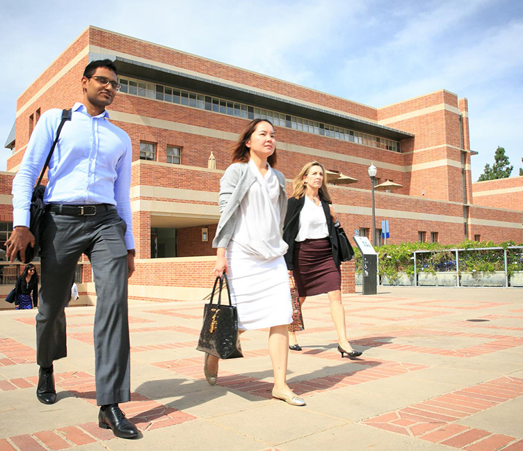 Three people walk in front of the School of Management building.