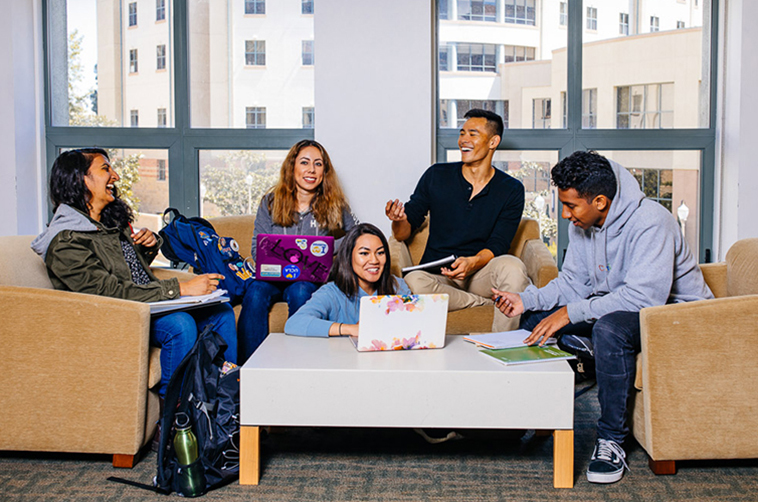 Five students laugh together in a residence hall common area.
