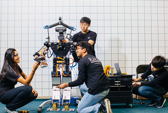 Four graduate students work together on a bipedal robot.