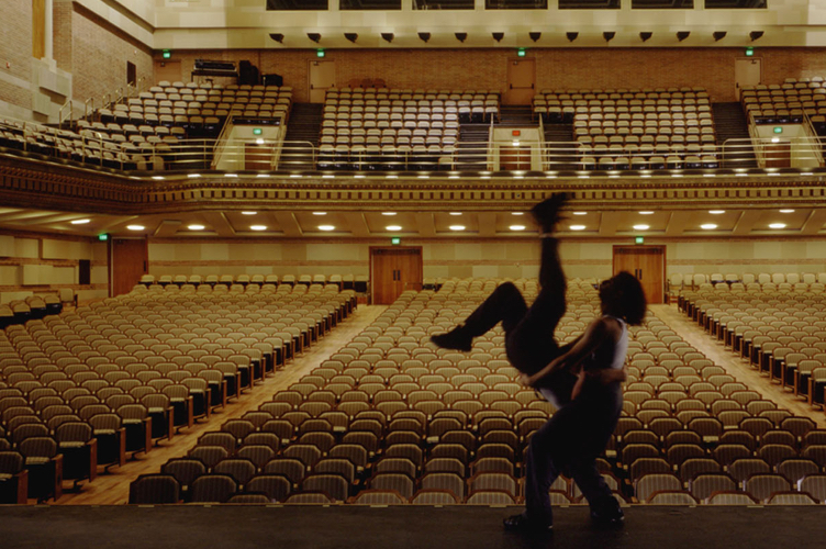 A blurry silhouette of two students as they rehearse to an empty audience hall.